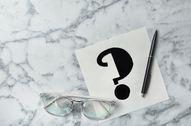 Note with question mark, eyeglasses and pen on white marble table, flat lay. Space for text