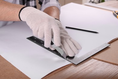 Worker cutting paper with utility knife and ruler at wooden table, closeup