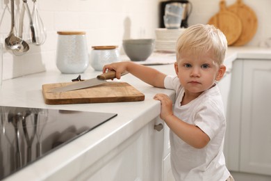 Curious little boy taking sharp knife from kitchen counter