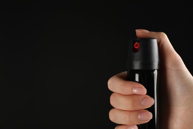 Woman holding pepper spray on black background, closeup. Space for text