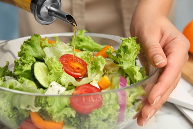 Woman dressing tasty fresh Greek salad with olive oil at table, closeup
