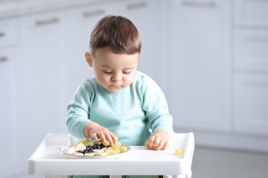 Cute little baby eating healthy food in high chair at home. Space for text