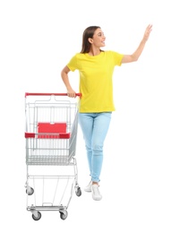 Young woman with empty shopping cart on white background