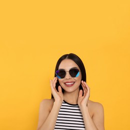 Attractive happy woman in fashionable sunglasses against orange background