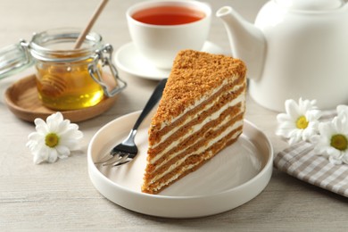 Photo of Slice of delicious layered honey cake served with tea on wooden table
