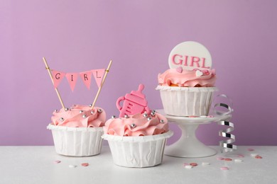 Baby shower cupcakes with pink cream and toppers on white table against violet background
