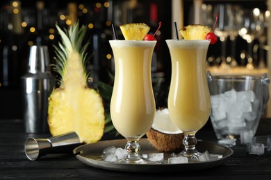 Tasty Pina Colada cocktails and ingredients on black wooden bar countertop