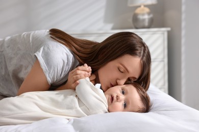 Photo of Happy mother kissing her little baby on bed at home