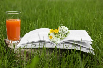 Photo of Open book with flowers and glass of juice on green grass outdoors