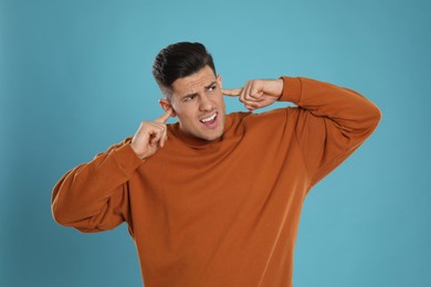 Emotional man covering ears with fingers on light blue background