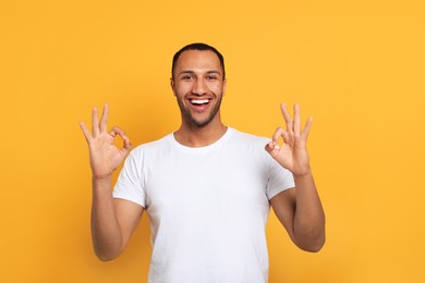 Photo of Smiling African American man showing ok gesture on orange background