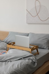 Wooden tray table with laptop and smartphone on bed indoors