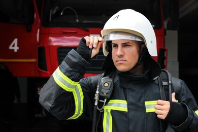Portrait of firefighter in uniform and helmet near fire truck at station