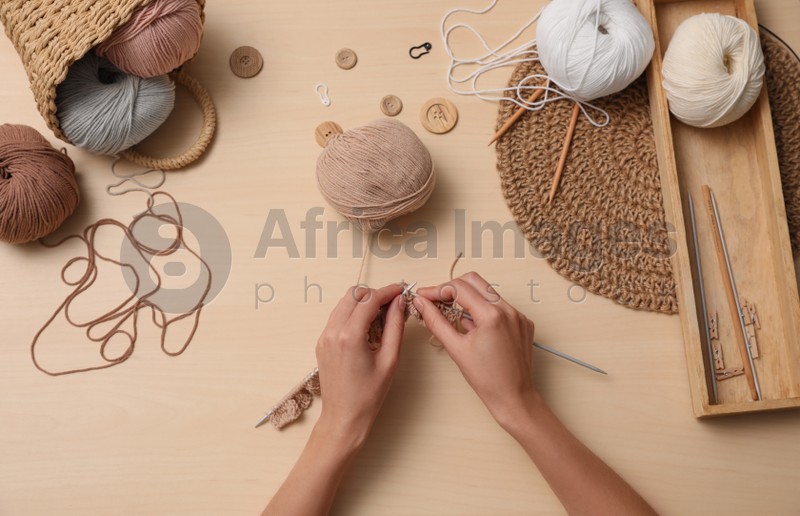 Woman knitting with threads at wooden table, top view. Engaging hobby