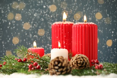 Snow falling on burning candles, fir branches and pine cones against blurred festive lights, space for text. Christmas eve