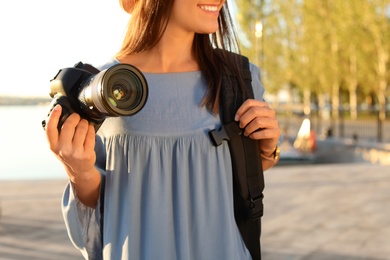 Young female photographer holding professional camera at pier