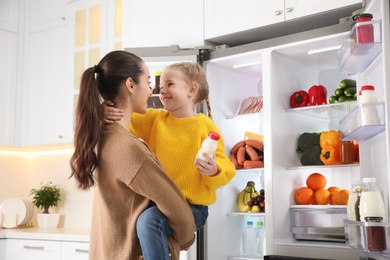 Young mother and daughter near open refrigerator in kitchen