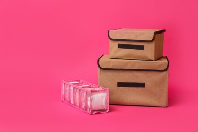 Textile storage cases and organizer with folded clothes on pink background. Space for text