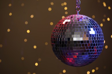 Shiny disco ball against blurred lights on brown background, space for text