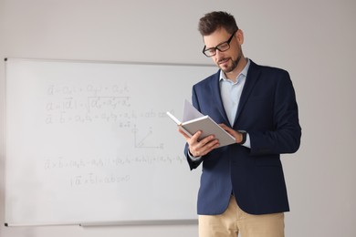 Photo of Teacher with book at whiteboard in classroom during math lesson
