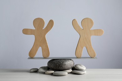 Balancing wooden human figures on stones against light grey background