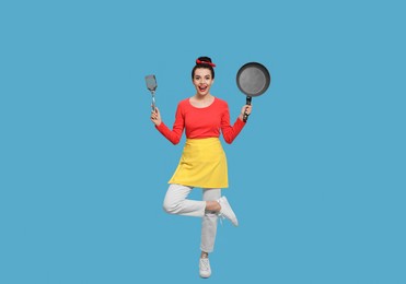 Photo of Housewife with frying pan and spatula on light blue background