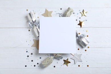Flat lay composition of Christmas crackers, shiny confetti and blank paper on white wooden background. Space for text