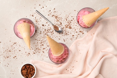 Flat lay composition with delicious pink ice cream in wafer cones, chocolate and almonds on light table