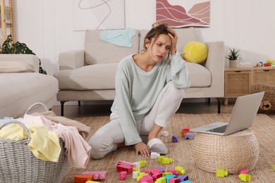 Tired young mother sitting on floor in messy living room