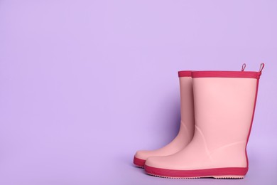 Pair of pink rubber boots on violet background. Space for text
