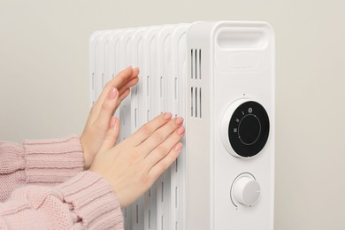 Photo of Young woman warming hands near modern electric heater on beige background, closeup