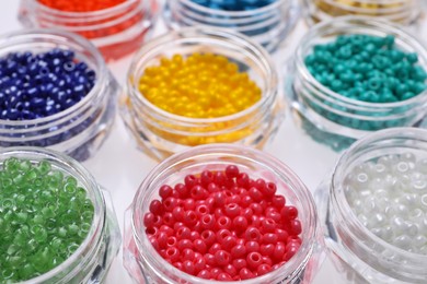 Plastic containers with different beads on white background, closeup