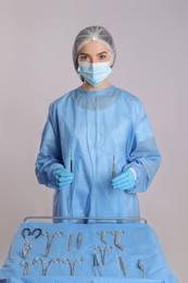 Doctor holding surgical instruments near table on light background