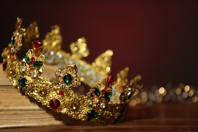 Beautiful golden crown and fairy lights on wooden table, closeup. Fantasy item