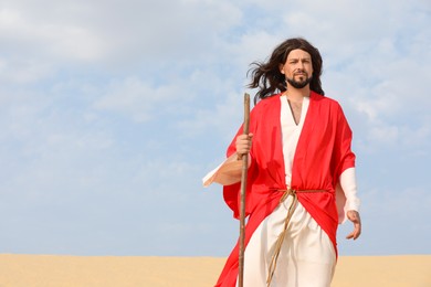 Jesus Christ walking with stick in desert. Space for text