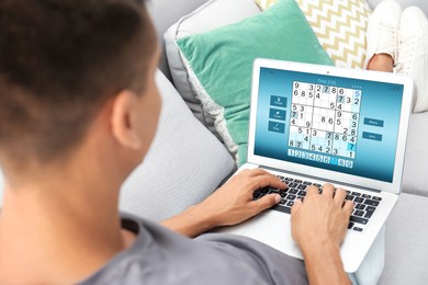 Man playing sudoku game on laptop indoors, closeup