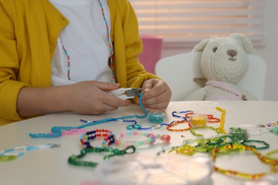 Little girl making beaded jewelry at table in room, closeup