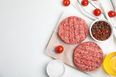 Raw hamburger patties with spices and tomatoes on white table, flat lay. Space for text