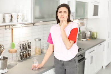 Young woman with sensitive teeth and glass of cold water in kitchen