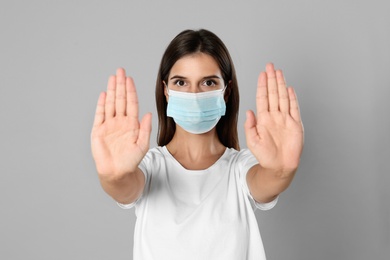 Woman in protective mask showing stop gesture on grey background. Prevent spreading of coronavirus
