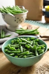 Fresh green beans in bowl on wooden table, closeup. Space for text