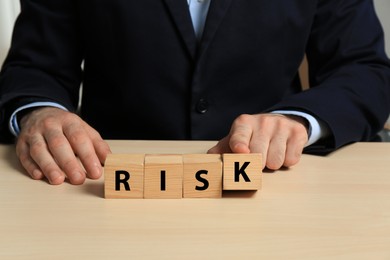 Businessman making word Risk of cubes at wooden table, closeup