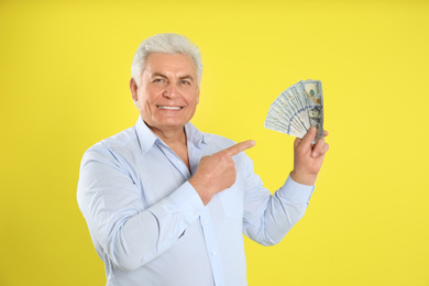 Happy senior man with cash money on yellow background