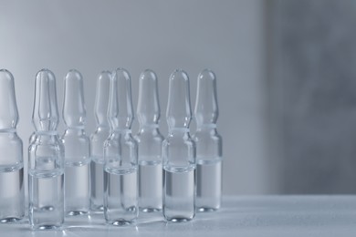 Pharmaceutical ampoules with medication on white table against grey background. Space for text