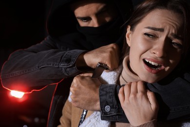 Criminal with knife attacking young woman outdoors at night. Self defense concept