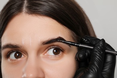 Beautician applying tint during eyebrows correction procedure on grey background, closeup
