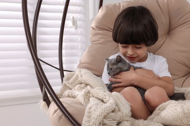 Photo of Cute little boy with kitten in hanging chair at home. Childhood pet