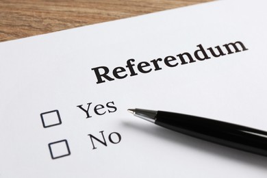 Referendum ballot with pen on wooden table, closeup