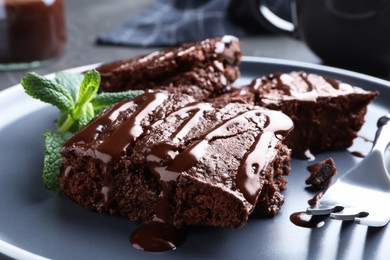 Delicious chocolate brownies with sweet syrup and mint on plate, closeup