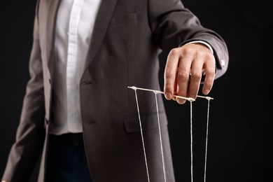 Man in suit pulling strings of puppet on black background, closeup